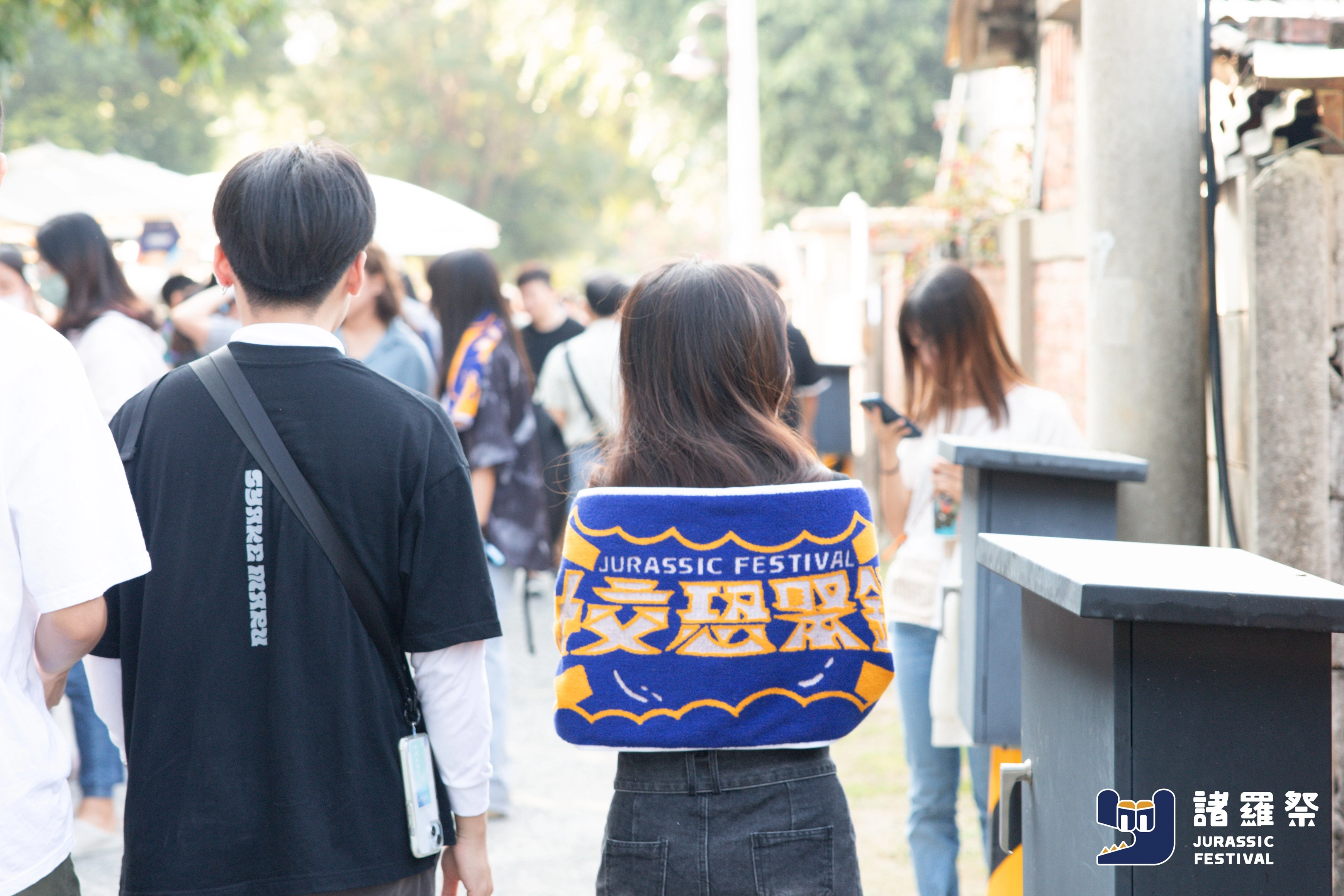 觀眾在諸羅祭 Jurassic Festival 現場披著品牌毛巾行走於人群中，呈現品牌自然融入線下活動的互動氛圍，體現行銷整合的真實現場感。